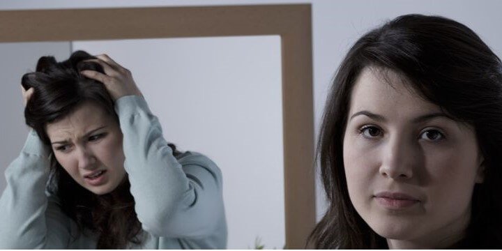 Young woman looking in a mirror struggling with mental health