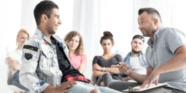 Young man sharing with therapist during group therapy in front of others