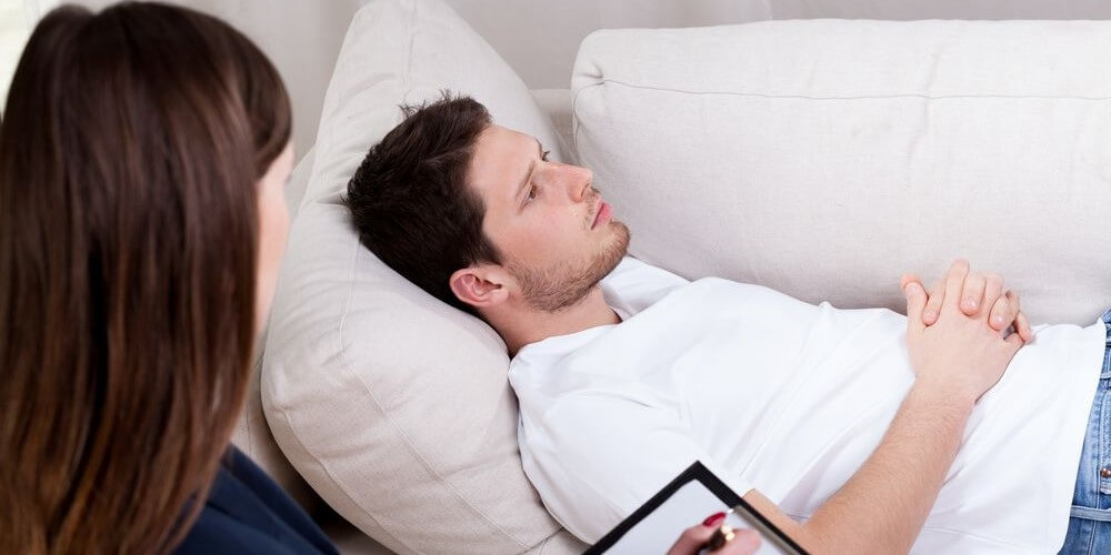 Young man on a couch during a therapy session with a woman psychologist