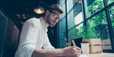 Man writing in notebook in front of windows