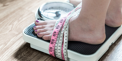 Person standing on scale and tied down by tape measure.